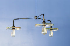 Close-up of a black modern ceiling light fixture with three circular lampshades embedded with pressed leaves and greenery, creating a bright and artistic design against a white background.