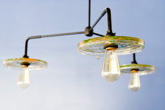 Close-up of a modern ceiling light fixture with three circular lampshades embedded with pressed leaves and greenery, creating a bright and artistic design against a white background.