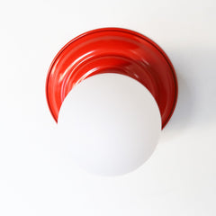 Poppy Orange Red Retro Style  flushmount ceiling light or wall sconce with a frosted white globe.  Stepping back into a bygone era with a touch of modern minimalism, the Abeille Sconce or Flushmount is an artistic blend of form and function. This wall sconce doubles as a flushmount ceiling light, making it a versatile lighting solution for any space. Designed akin to a beehive, its charismatic shape is complemented by curated color options that add a playful element to its retro appeal.