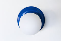 Bright Blue flushmount ceiling light or wall sconce with a frosted white globe.  Stepping back into a bygone era with a touch of modern minimalism, the Abeille Sconce or Flushmount is an artistic blend of form and function. This wall sconce doubles as a flushmount ceiling light, making it a versatile lighting solution for any space. Designed akin to a beehive, its charismatic shape is complemented by curated color options that add a playful element to its retro appeal.