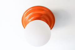 Stepping back into a bygone era with a touch of modern minimalism, the Abeille Sconce or Flushmount  in bright orange is an artistic blend of form and function. This wall sconce doubles as a flushmount ceiling light, making it a versatile lighting solution for any space. Designed akin to a beehive, its charismatic shape is complemented by curated color options that add a playful element to its retro appeal.