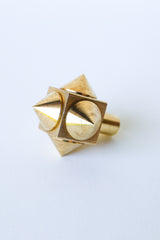 Close-up of a raw brass spike cube knob with a bold, geometric design, featuring four rounded brass spikes on a solid brass cube base.