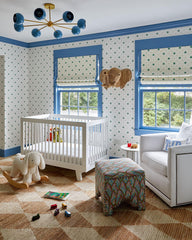 Boys nursery with Arcenciel Chandelier in hydrangea blue by Sazerac Stitches, white crib, woven rug, wicker elephant wall decor, and playful star wallpaper with blue trim. Modern colorful chandelier lighting for kids’ rooms.