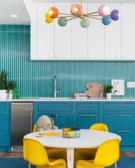 Pastel Rainbow Chandelier in a turquoise and teal kitchen with kids table and bright yellow chairs. High end playroom design