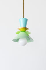 A close-up of the Astro Pendant by Sazerac Stitches, highlighting its powder-coated metal shades in aqua blue, vibrant lime green, and soft mint green, stacked in a unique, retro-inspired arrangement. The fixture is finished with a brass accent and a white globe bulb for a bold, artistic touch.