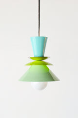 The Astro Pendant light by Sazerac Stitches in a fresh colorway featuring powder-coated finishes in aqua blue, bright lime green, and soft mint green. This playful, geometric lighting fixture is suspended from a brass rod, creating a modern, sculptural statement for any space.