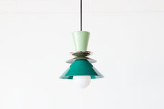 Close-up of the Astro Pendant in Vista Green, Olive Green, and Mermaid Green. This mid-century modern-inspired pendant features a playful combination of colors, with a glossy green top cone, metallic dish accents, and layered conical shades, suspended from a sleek rod.