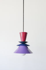 Astro pendant light featuring a bold colorblocked design in Black Cherry, Navy, and Orchid. This sculptural ceiling light is handcrafted with powder-coated metal in a tiered, mid-century modern inspired silhouette. A striking and vibrant choice for kitchens, dining spaces, or eclectic interiors, it brings playful sophistication and a pop of color to maximalist and design-forward homes. Ideal as a single statement piece or grouped over an island.