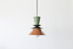 Astro pendant light in olive green, black, and fudge brown with brass accent. A colorblocked mid century modern ceiling fixture with earthy, moody tones. Ideal for warm, vintage-inspired kitchens, eclectic dining rooms, or modern rustic interiors. A bold and timeless lighting choice for statement design lovers.