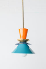 Colorblocked Astro Pendant light featuring bold, powdercoated aluminum shades in vibrant orange peel, rich denim blue, and saturated teal. Accented with a brass detail and suspended from a brass rod. This geometric ceiling light by Sazerac Stitches is handmade in New Orleans and ideal for maximalist, eclectic, or color-forward kitchen designs.