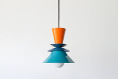 Colorblocked Astro Pendant light featuring bold, powdercoated aluminum shades in vibrant orange peel, rich denim blue, and saturated teal. Accented with a brass detail and suspended from a brass rod. This geometric ceiling light by Sazerac Stitches is handmade in New Orleans and ideal for maximalist, eclectic, or color-forward kitchen designs.