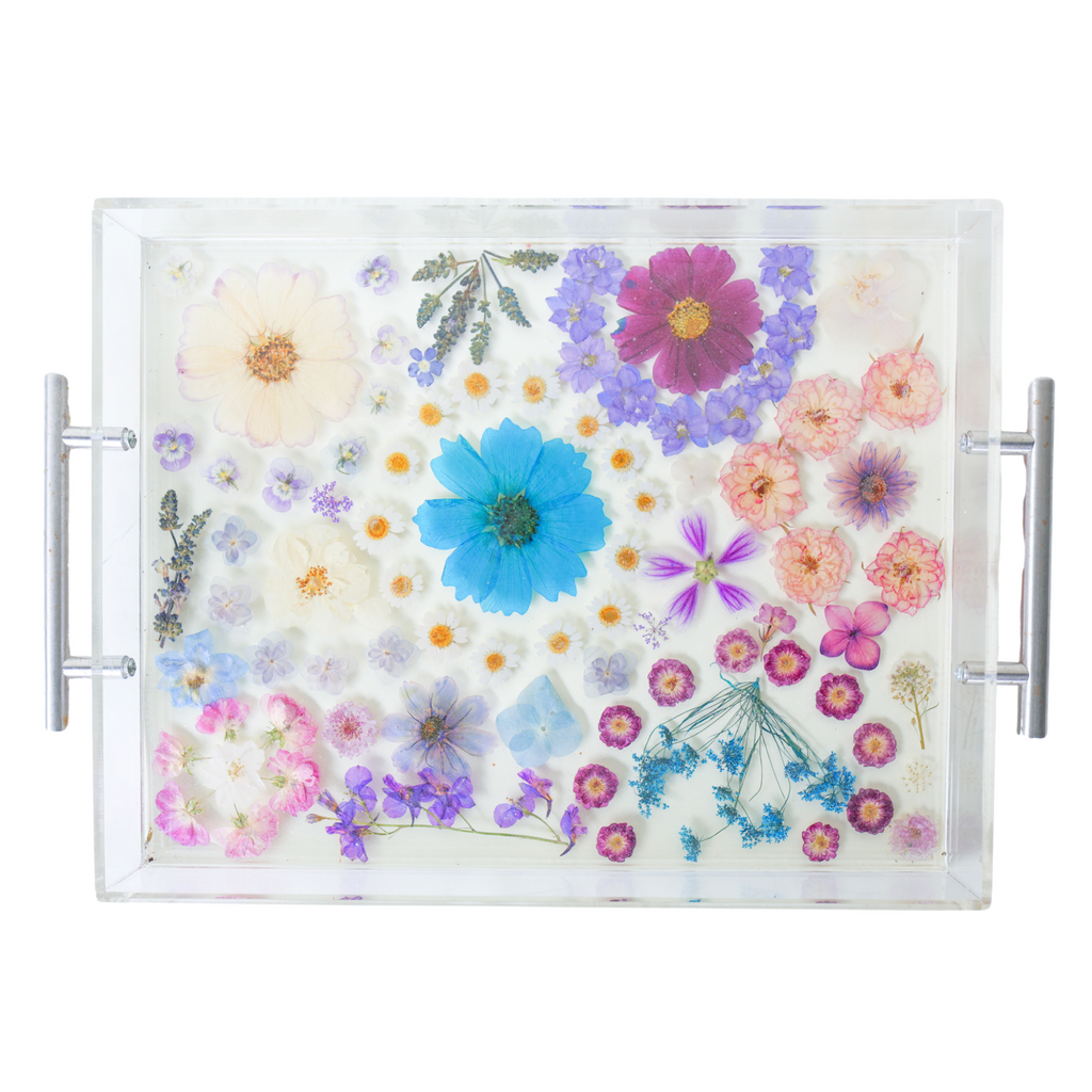 Handmade acrylic tray with clear resin base and silver metal handles, featuring an intricate arrangement of real pressed flowers in soft pastels and rich jewel tones. The floral composition includes daisies, violets, cosmos, hydrangeas, and roses in a palette of purples, blues, lavenders, and blush pinks. The vibrant blossoms are carefully preserved in a dreamy, organic layout, creating a romantic, nature-inspired serving tray or decorative catchall perfect for spring, gift giving, or adding a whimsical tou