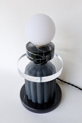 Modern one-of-a-kind lamp featuring a spherical frosted glass globe, vintage reclaimed black marble component, transparent acrylic disc, and a matte black ceramic fluted base resting on a polished black marble platform; handmade statement lighting piece with bold materials and geometric form