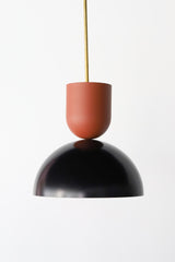 Close-up of the Taeuber Pendant in terra cotta and black by Sazerac Stitches, featuring a glossy two-tone powder-coated finish and brass downrod. This sculptural pendant light showcases minimalist curves and handcrafted detailing, blending midcentury modern design with a soft, neutral palette. Perfect for kitchens, dining rooms, or entryways, this artisan-made fixture adds a timeless and elegant touch to both contemporary and classic interiors.