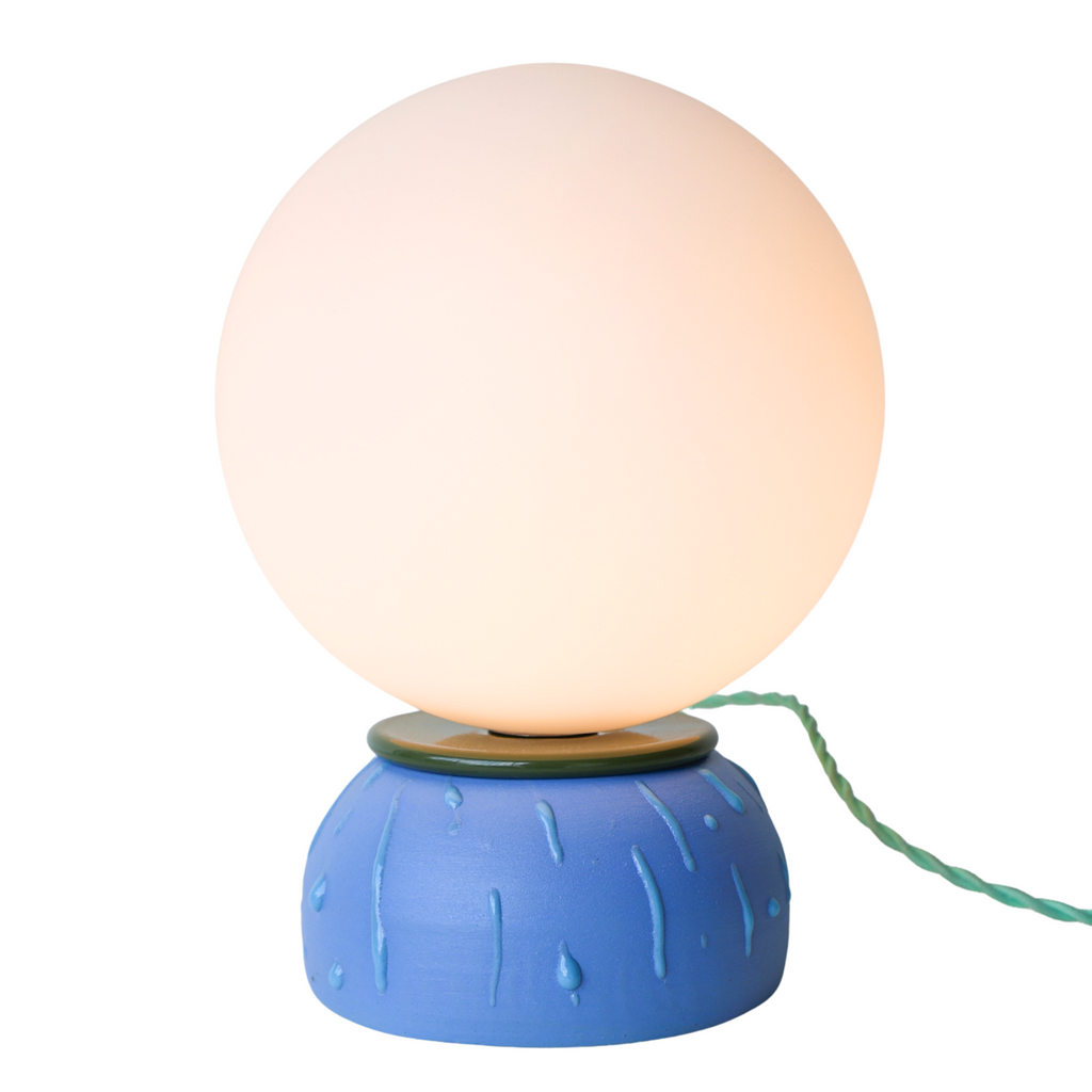 One-of-a-kind Olive and Blue Drip ceramic table lamp featuring a matte blue base with raised drip texture, olive green rim, and a glowing white glass globe shade. Handmade modern artisan lighting, perfect for a colorful desk lamp, nightstand lamp, or accent light in eclectic, modern, or mid-century interiors.