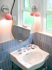 pastel bathroom remodel featuring a chrome and porcelain sink, pastel pink and chrome wall sconces, pastel blue wall tile, and a green penny tile flooring. Bautiful pastel bathroom remodel
