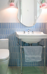 pastel bathroom remodel featuring a chrome and porcelain sink, pastel pink and chrome wall sconces, pastel blue wall tile, and a green penny tile flooring. Bautiful pastel bathroom remodel