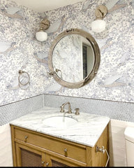 Neutral bathroom remodel features patterned fish wallpaper, chrome porthole mirror, and white chrome sconces with vintage style schoolhouse glass shades