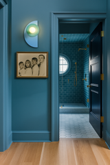 Color-drenched, monochromatic blue bedroom hallway with saturated blue walls and ceiling, featuring bold wall lighting from our Kin Sconce in layered green and blue tones; space leads into a cohesive tonal bathroom with deep blue tile, warm brass fixtures, and thoughtfully coordinated color blocking, blending modern design with playful, eclectic styling.
