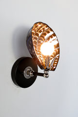 Handmade Coquille Sconce illuminated, showcasing shimmering iridescent ceramic shell in black with glowing copper and purple accents, silver leaf detail, and silver-tone vintage hardware; one-of-a-kind Art Deco-inspired light fixture