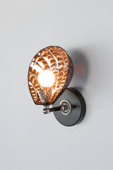 Handmade Coquille Sconce illuminated, showcasing shimmering iridescent ceramic shell in black with glowing copper and purple accents, silver leaf detail, and silver-tone vintage hardware; one-of-a-kind Art Deco-inspired light fixture