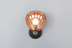 Artistic shell-shaped wall sconce glowing warmly, with hand-painted ceramic in glossy black and iridescent finish, featuring silver-toned leaf element and hardware; custom ambient light from Sazerac Stitches’ One of One collection