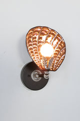 Handmade Coquille Sconce illuminated, showcasing shimmering iridescent ceramic shell in black with glowing copper and purple accents, silver leaf detail, and silver-tone vintage hardware; one-of-a-kind Art Deco-inspired light fixture