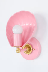 Coquille sconce in blush pink with brass details, featuring a sculptural shell-shaped design inspired by vintage Art Deco and coastal interiors. This elegant wall light blends timeless glamour with playful charm, ideal for bedrooms, nurseries, hallways, or living spaces. The soft pastel pink finish complements maximalist, eclectic, or Nancy Meyers-style interiors while adding a whimsical touch. Handcrafted and available in over 30 custom colors, this unique shell wall sconce offers the perfect ambient glow