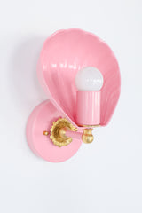 Coquille sconce in blush pink with brass details, featuring a sculptural shell-shaped design inspired by vintage Art Deco and coastal interiors. This elegant wall light blends timeless glamour with playful charm, ideal for bedrooms, nurseries, hallways, or living spaces. The soft pastel pink finish complements maximalist, eclectic, or Nancy Meyers-style interiors while adding a whimsical touch. Handcrafted and available in over 30 custom colors, this unique shell wall sconce offers the perfect ambient glow