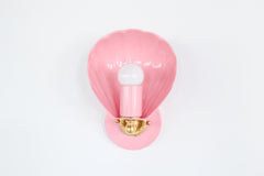 Coquille sconce in blush pink with brass details, featuring a sculptural shell-shaped design inspired by vintage Art Deco and coastal interiors. This elegant wall light blends timeless glamour with playful charm, ideal for bedrooms, nurseries, hallways, or living spaces. The soft pastel pink finish complements maximalist, eclectic, or Nancy Meyers-style interiors while adding a whimsical touch. Handcrafted and available in over 30 custom colors, this unique shell wall sconce offers the perfect ambient glow
