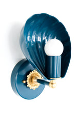 Shell-shaped wall sconce with a powdercoated lagoon blue finish and solid brass accents, including a detailed rosette and finial. The sconce features a sculptural shell form that cradles a bulb, casting soft ambient light. Shown from multiple angles on a white background, this coastal-inspired light fixture blends vintage Art Deco design with contemporary elegance, ideal for bedrooms, bathrooms, hallways, and eclectic interiors.