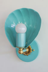 Shell-shaped wall sconce light fixture in a light aqua blue color with cast brass details.  Nancy Meyers aesthetic that also works with coastal or chinoiserie styled interiors.  Powdercoated steel with brass accents. Perfect wall sconce for powder rooms, bathrooms, and more.  Adds a little bit of fun whimsy with the nautical shell shape of the sconce.