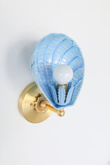 Detailed close-up of celestial blue Coquille scallop shell wall light fixture with intricate cream brushstrokes and leafy painted socket cup, brass base, and soft reflective finish