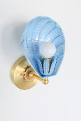 Detailed close-up of celestial blue Coquille scallop shell wall light fixture with intricate cream brushstrokes and leafy painted socket cup, brass base, and soft reflective finish