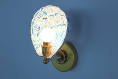 Top-down view of the hand-painted Coquille sconce featuring a sculptural powder-coated steel shade shaped like a fan shell, painted with vibrant cobalt blue lines and accents. Centered is a white globe bulb seated in a vintage-style fluted brass socket, affixed to a polished brass backplate with floral detailing. The design offers a blend of nautical inspiration and classic French opulence, perfect for eclectic and colorful interiors.