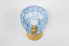 Scalloped white and blue wall sconce with hand-painted brushstroke detailing on a powder-coated steel shell-shaped shade, attached to a solid brass round wall plate with floral rosette and decorative socket. The crisp white background emphasizes the vibrant cobalt strokes and detailed craftsmanship, ideal for showcasing this one-of-a-kind artisan sconce as a bold lighting statement for bathrooms, hallways, or bedrooms.