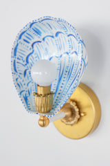 Top-down view of the hand-painted Coquille sconce featuring a sculptural powder-coated steel shade shaped like a fan shell, painted with vibrant cobalt blue lines and accents. Centered is a white globe bulb seated in a vintage-style fluted brass socket, affixed to a polished brass backplate with floral detailing. The design offers a blend of nautical inspiration and classic French opulence, perfect for eclectic and colorful interiors.