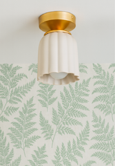 Cream Marcella Flushmount ceiling light by Sazerac Stitches, featuring a scalloped ceramic shade and brass base, styled on a white ceiling with soft green fern botanical wallpaper for a fresh, nature-inspired interior look.