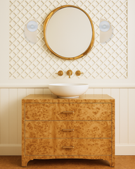 Cream-toned bathroom with modern wainscoting and decorative lattice paneling, featuring a burl wood vanity with brushed brass hardware, a round gold-framed mirror, and a pair of sculptural Kin Sconces in pale yellow and soft white. This elegant vanity setup combines warm wood textures with soft lighting and minimalist color blocking, perfect for a transitional or modern classic bathroom design.