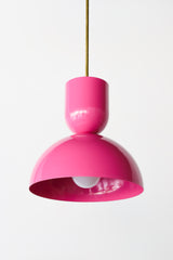 Close-up of the Taeuber Pendant in bright Doll Pink by Sazerac Stitches, showcasing its sculptural double-dome silhouette and glossy powder-coated finish with a brass downrod. This modern, handmade pendant light highlights the bold color and smooth craftsmanship of the design, perfect for kitchens, dining nooks, and modern interiors seeking a pop of color and midcentury-inspired style.