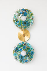 Modern two light wall sconce with brass hardware. Features resin-encapsulated greenery, ferns, and leaves.  Adds a real-like nature theme to any interior design project.  Called the Botanico Sconce by Sazerac Stitches. Features blue & white flowers with white greenery