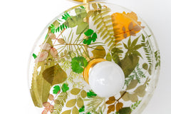 Modern two light wall sconce with brass hardware. Features resin-encapsulated greenery, ferns, and leaves.  Adds a real-like nature theme to any interior design project.  Called the Botanico Sconce by Sazerac Stitches. Features green and yellow leaves & greenery