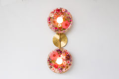 Modern two light wall sconce with brass hardware and pink & purple flowers. Features resin-encapsulated pink & purple flowers with greenery, ferns, and leaves.  Adds a real-like nature theme to any interior design project.  Called the Botanico Sconce by Sazerac Stitches. Features pink & purple flowers with greenery