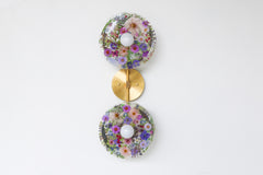 Modern two light wall sconce with brass hardware and purple flowers. Features resin-encapsulated purple flowers with greenery, ferns, and leaves.  Adds a real-like nature theme to any interior design project.  Called the Botanico Sconce by Sazerac Stitches. Features purple flowers with greenery