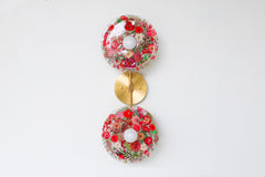 Modern two light wall sconce with brass hardware and red flowers. Features resin-encapsulated pink & purple flowers with greenery, ferns, and leaves.  Adds a real-like nature theme to any interior design project.  Called the Botanico Sconce by Sazerac Stitches. Features red flowers with greenery