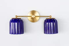 Front-facing product image of the Double Marcella Sconce in cobalt blue ceramic with ridged scalloped shades and a polished brass arm and backplate. Designed and made in the USA by Sazerac Stitches, this feminine yet bold Art Deco wall light is perfect for bathroom vanities, eclectic interiors, or color-drenched design schemes.