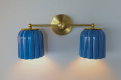 Handmade Double Marcella Sconce featuring sculptural ribbed ceramic shades in glazed cobalt-sky blue and solid brass mount, wall light casting ambient glow for art deco, maximalist, and eclectic home decor