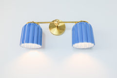 Double Marcella Sconce illuminated with sky blue fluted ceramic shades casting soft downward light, handcrafted brass and ceramic wall fixture perfect for vanity lighting, bedside sconces, or hallway uplighting