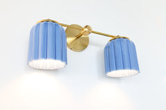 Sazerac Stitches Double Marcella ceramic wall sconce in glazed sky blue with brass hardware, ribbed fluted shades glowing downward, handmade American lighting inspired by vintage glass and chinoiserie design