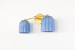 Marcella Double Wall Sconce with two sculptural ribbed ceramic shades in sky blue glaze and solid brass fixture arm, handmade artisan lighting designed for bathrooms, bedrooms, and entryways
